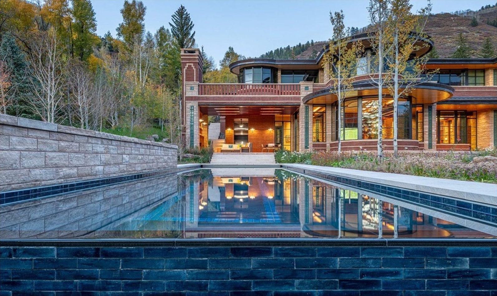 Modern residence at dusk with a reflecting infinity-edge pool, warm wood siding, and curved glass architecture