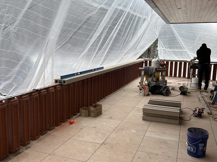 Under the mesh — stone handrail cap segments waiting on the floor while balusters go up.